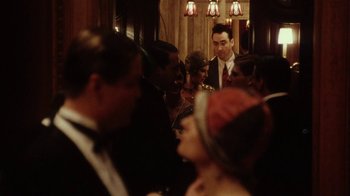 Movie still from “Bullets Over Broadway” (1994), directed by Woody Allen – A group of people standing in a room with a man in the middle; Medium shot, Over the shoulder angle