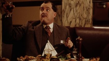 Movie still from “Bullets Over Broadway” (1994), directed by Woody Allen – A man sitting at a table with a plate of food in front of him; Medium shot, Low angle