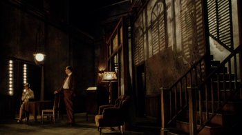 Movie still from “Bullets Over Broadway” (1994), directed by Woody Allen – A man standing in a dimly - lit room next to a chair; Wide shot, Low angle