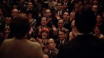 Movie still from “Bullets Over Broadway” (1994), directed by Woody Allen – A group of people sitting in a room clapping; Medium shot, High angle
