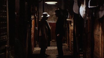 Movie still from “Bullets Over Broadway” (1994), directed by Woody Allen – Two men standing in a dark room with a light shining on them; Wide shot, High angle