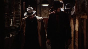 Movie still from “Bullets Over Broadway” (1994), directed by Woody Allen – Two men in suits and hats walking down a dark hallway; Medium shot, Low angle