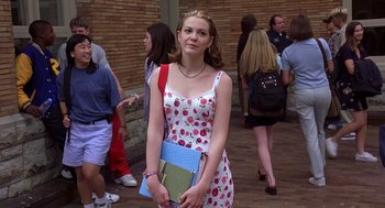 Movie still from “10 Things I Hate About You” (1999), directed by Gil Junger – A woman in a dress holding a book and a purse; Medium shot, High angle