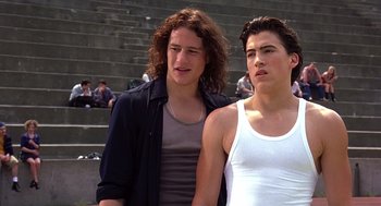 Movie still from “10 Things I Hate About You” (1999), directed by Gil Junger – Two young men standing next to each other in front of an amphitheater; Medium shot, Low angle