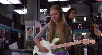 Movie still from “10 Things I Hate About You” (1999), directed by Gil Junger – A woman is playing a guitar in a store; Medium shot, Low angle