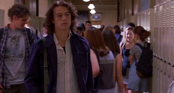 Movie still from “10 Things I Hate About You” (1999), directed by Gil Junger – A man with curly hair is standing in a hallway; Medium shot, Over the shoulder angle