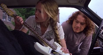 Movie still from “10 Things I Hate About You” (1999), directed by Gil Junger – A woman sitting in the back of a car next to a man holding a guitar; Medium shot, Low angle