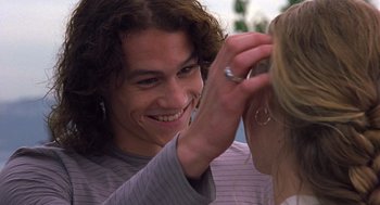 Movie still from “10 Things I Hate About You” (1999), directed by Gil Junger – A man smiling at a woman's ear while she puts a ring on it's ear; Close Up shot, Over the shoulder angle