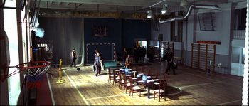 Movie still from “12” (2007), directed by Nikita Mikhalkov – People are walking around a room with tables and chairs; Extreme Wide shot, High angle