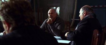 Movie still from “12” (2007), directed by Nikita Mikhalkov – An older man sitting at a dining room table; Medium shot, Over the shoulder angle