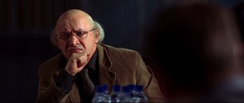Movie still from “12” (2007), directed by Nikita Mikhalkov – An older man sitting in front of water bottles; Close Up shot, Over the shoulder angle