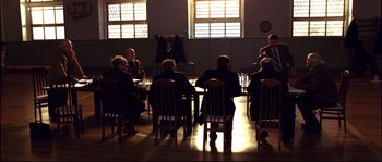 Movie still from “12” (2007), directed by Nikita Mikhalkov – A group of people sitting at a table in a room; Wide shot, High angle