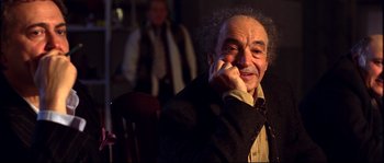 Movie still from “12” (2007), directed by Nikita Mikhalkov – An older man sitting in a chair talking on a cell phone; Close Up shot, Over the shoulder angle