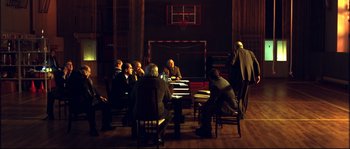 Movie still from “12” (2007), directed by Nikita Mikhalkov – A group of people sitting around a table in a room; Wide shot, High angle