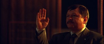 Movie still from “12” (2007), directed by Nikita Mikhalkov – A man in a suit raises his hand in the dark; Close Up shot, Over the shoulder angle