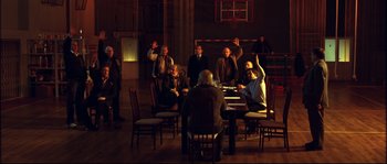 Movie still from “12” (2007), directed by Nikita Mikhalkov – A group of people sitting around a table in a room; Wide shot, High angle