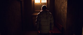 Movie still from “12” (2007), directed by Nikita Mikhalkov – A man in a jacket standing in a dark room; Wide shot, Low angle
