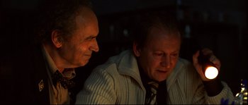 Movie still from “12” (2007), directed by Nikita Mikhalkov – Two men are sitting in a dimly lit room; Close Up shot, High angle