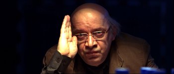 Movie still from “12” (2007), directed by Nikita Mikhalkov – A bald man in a brown jacket holding his hand up to his face; Close Up shot, Over the shoulder angle
