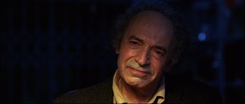 Movie still from “12” (2007), directed by Nikita Mikhalkov – An older man with a beard and curly hair looking at the camera; Close Up shot, Over the shoulder angle
