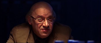 Movie still from “12” (2007), directed by Nikita Mikhalkov – An older man wearing glasses and a jacket; Close Up shot, Over the shoulder angle