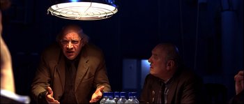 Movie still from “12” (2007), directed by Nikita Mikhalkov – Two older men sitting at a table in front of a light fixture; Medium shot, Over the shoulder angle