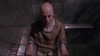 Movie still from “12 Monkeys” (1995), directed by Terry Gilliam – A bald man sitting on a chair with his hands chained; Medium shot, High angle