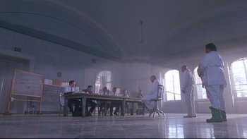 Movie still from “12 Monkeys” (1995), directed by Terry Gilliam – A group of people sitting around a table in a room; Wide shot, Low angle