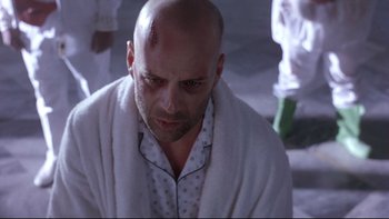 Movie still from “12 Monkeys” (1995), directed by Terry Gilliam – A man with a shaved head and a towel around his neck; Close Up shot, Low angle
