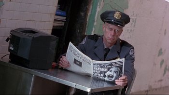 Movie still from “12 Monkeys” (1995), directed by Terry Gilliam – A police officer sitting at a table reading a newspaper; Medium shot, Low angle