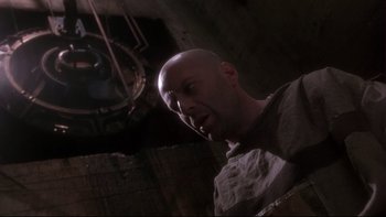 Movie still from “12 Monkeys” (1995), directed by Terry Gilliam – A bald man with a shaved head is looking at the camera; Medium shot, Low angle