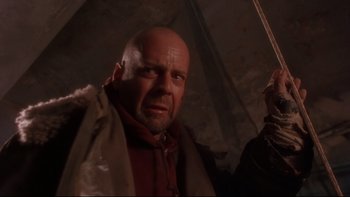 Movie still from “12 Monkeys” (1995), directed by Terry Gilliam – A bald man with a beard and a red shirt is holding an umbrella; Close Up shot, Low angle