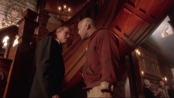 Movie still from “12 Monkeys” (1995), directed by Terry Gilliam – Two men are talking in front of a wooden staircase; Medium shot, Low angle