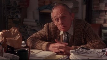 Movie still from “12 Monkeys” (1995), directed by Terry Gilliam – An older man sitting at a table in a room; Close Up shot, High angle