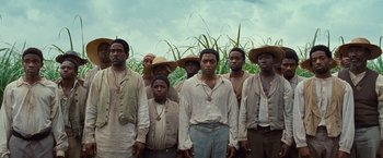 Movie still from “12 Years a Slave” (2013), directed by Steve McQueen – A group of men standing next to each other in a field; Wide shot, Low angle