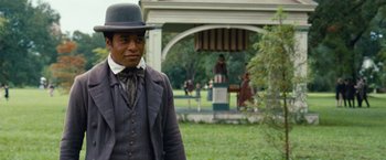 Movie still from “12 Years a Slave” (2013), directed by Steve McQueen – A man wearing a black hat and a suit; Medium shot, Over the shoulder angle