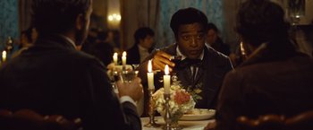 Movie still from “12 Years a Slave” (2013), directed by Steve McQueen – A man sitting at a dinner table holding a wine glass; Medium shot, Over the shoulder angle