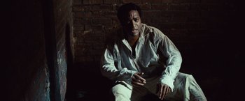 Movie still from “12 Years a Slave” (2013), directed by Steve McQueen – A man sitting on the ground in front of a brick wall; Medium shot, High angle