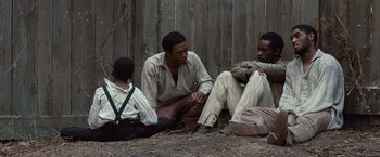 Movie still from “12 Years a Slave” (2013), directed by Steve McQueen – A group of men sitting next to each other on the ground; Medium shot, High angle