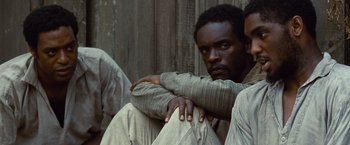 Movie still from “12 Years a Slave” (2013), directed by Steve McQueen – A man sitting on the ground with his hands on his knees; Close Up shot, Over the shoulder angle