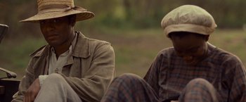 Movie still from “12 Years a Slave” (2013), directed by Steve McQueen – Two men sitting next to each other on the grass; Close Up shot, Over the shoulder angle
