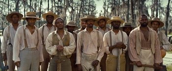 Movie still from “12 Years a Slave” (2013), directed by Steve McQueen – A group of men standing next to each other in a field; Wide shot, Low angle