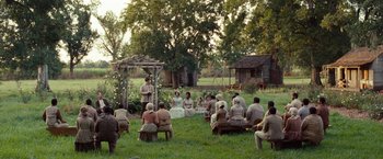 Movie still from “12 Years a Slave” (2013), directed by Steve McQueen – A group of people sitting in the grass with trees in the background; Extreme Wide shot, High angle