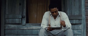 Movie still from “12 Years a Slave” (2013), directed by Steve McQueen – A man sitting on steps looking at a tablet computer; Medium shot, Low angle