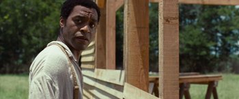 Movie still from “12 Years a Slave” (2013), directed by Steve McQueen – A man standing in front of a wooden structure; Close Up shot, Over the shoulder angle