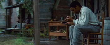 Movie still from “12 Years a Slave” (2013), directed by Steve McQueen – A man sitting on the ground using a cell phone; Medium shot, High angle