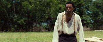 Movie still from “12 Years a Slave” (2013), directed by Steve McQueen – A man standing in the grass wearing a white shirt; Medium shot, Over the shoulder angle
