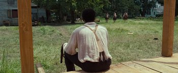 Movie still from “12 Years a Slave” (2013), directed by Steve McQueen – A man sitting on a bench in front of some horses; Wide shot, Over the shoulder angle