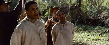 Movie still from “12 Years a Slave” (2013), directed by Steve McQueen – A group of men standing next to each other in the woods; Medium shot, Over the shoulder angle