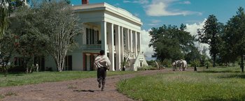 Movie still from “12 Years a Slave” (2013), directed by Steve McQueen – A man is running in front of a large white house; Extreme Wide shot, Low angle